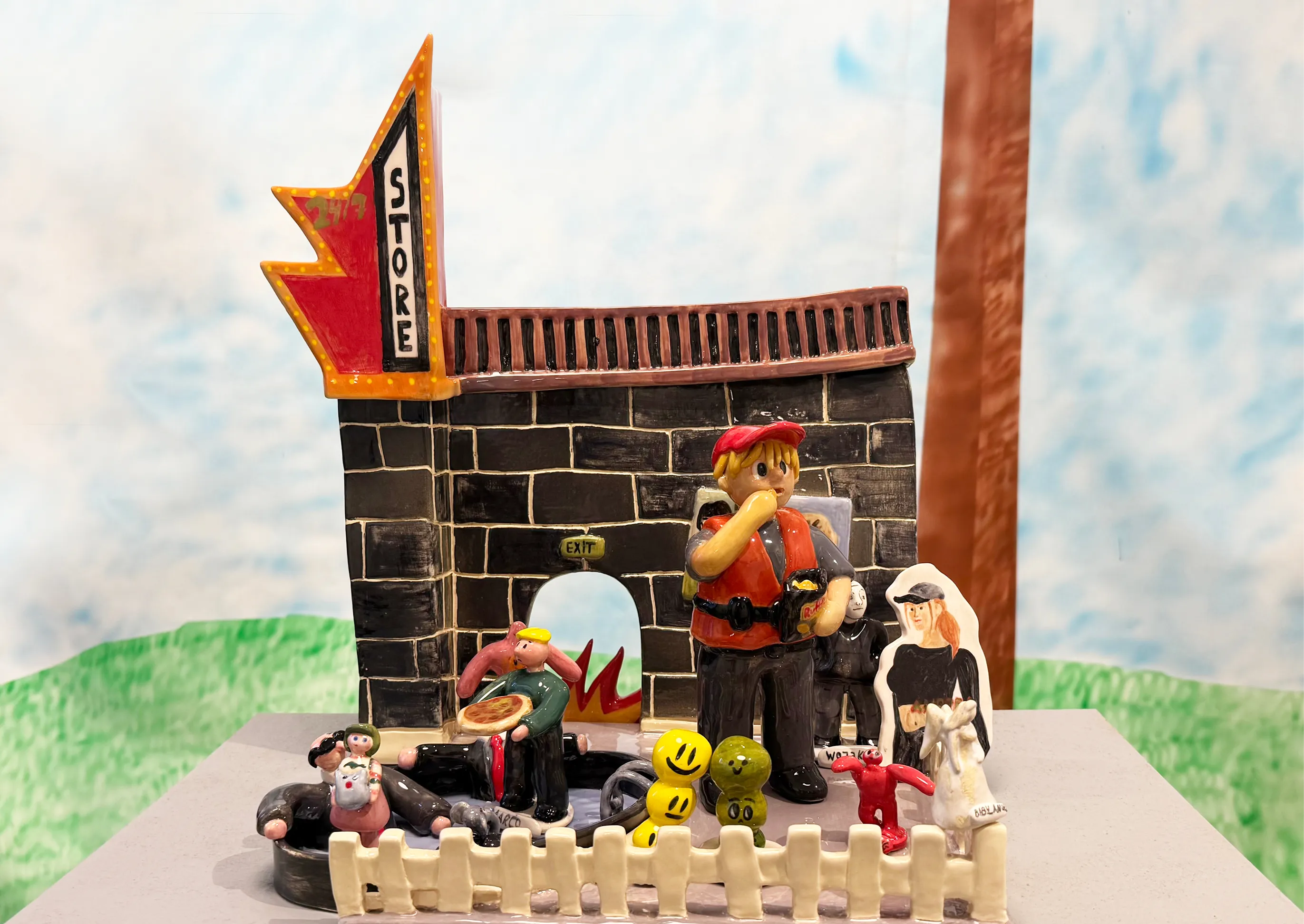 Glazed ceramic sculpture of a miniature corner store with tiny figures, set on a cinderblock pedestal