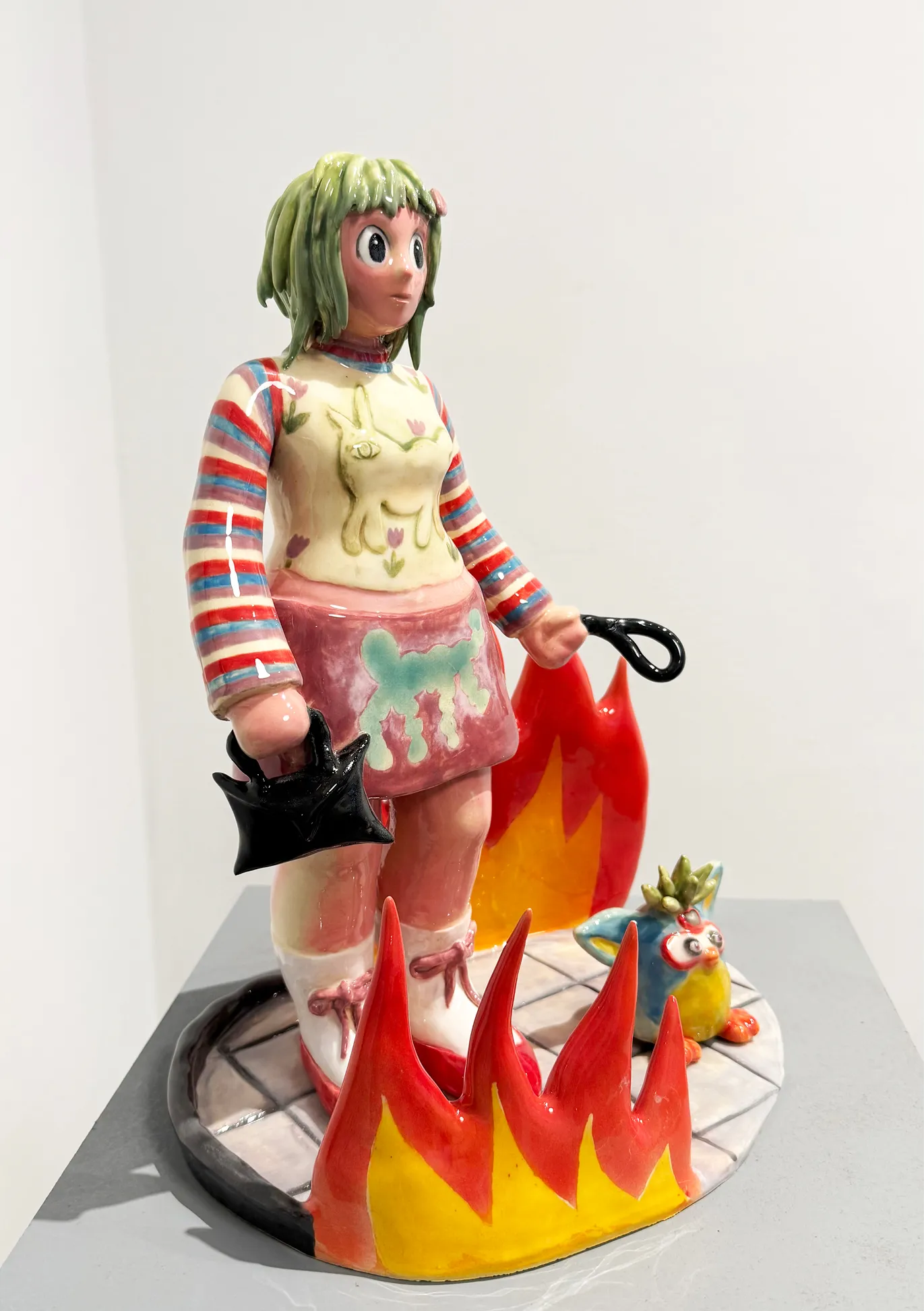 Ceramic figure of a girl with green hair standing amid flames, alongside a small furred creature