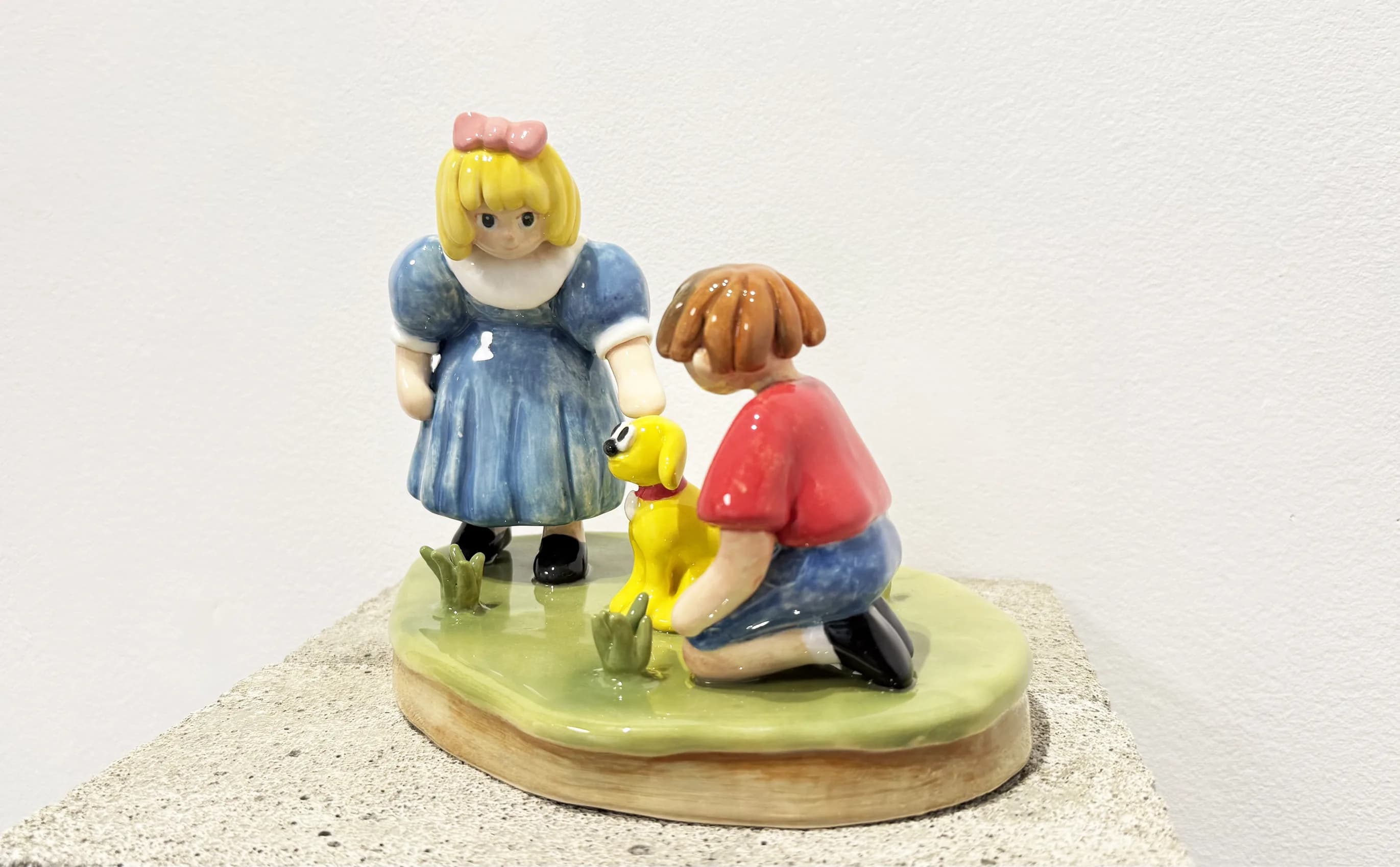 Holographic Pet seen from the front: a girl and a boy petting a yellow dog on a green glazed base