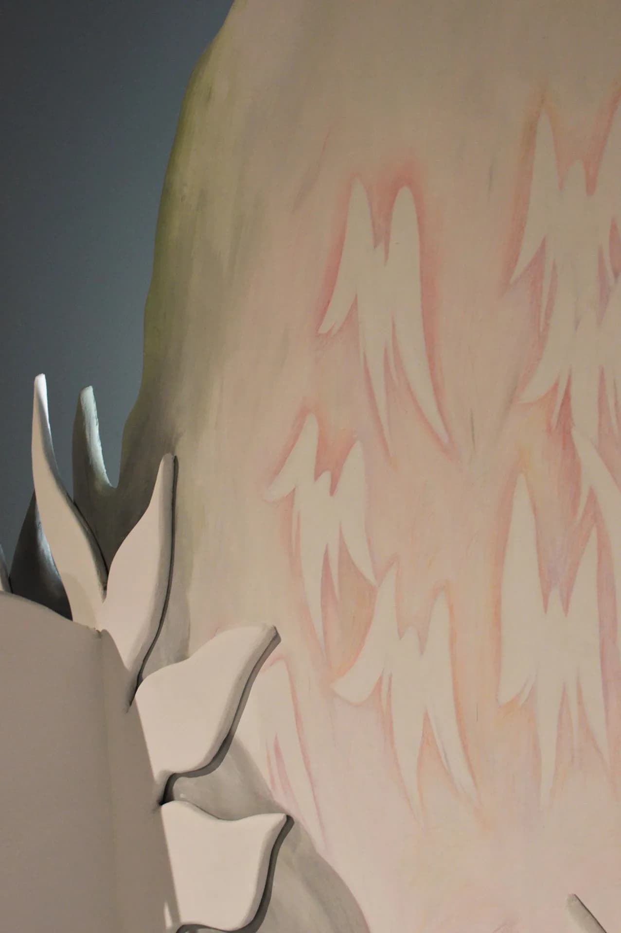 Close-up of a pale painted panel with pink feather-like brushstrokes behind white wave-shaped cutouts