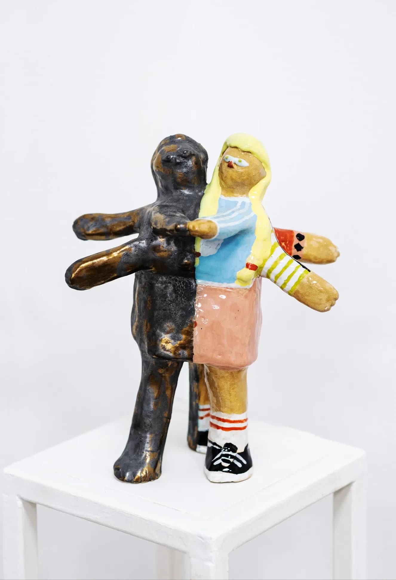 Two-tone ceramic sculpture of a dark glazed figure and a brightly painted figure standing back to back