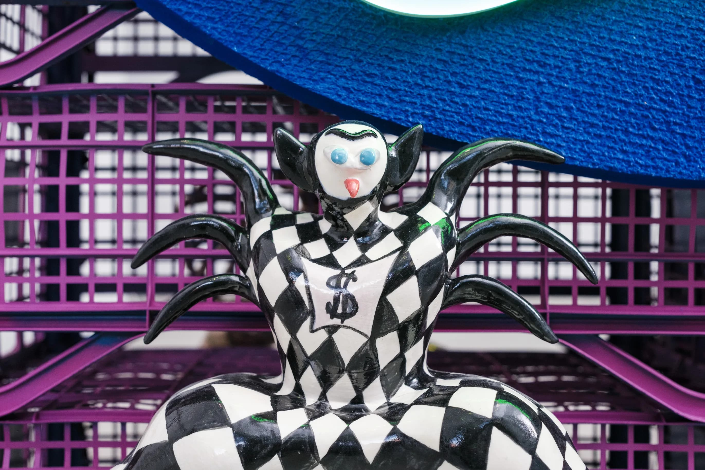 Detail of a black and white harlequin-patterned figure with spiky arms beneath the neon sign