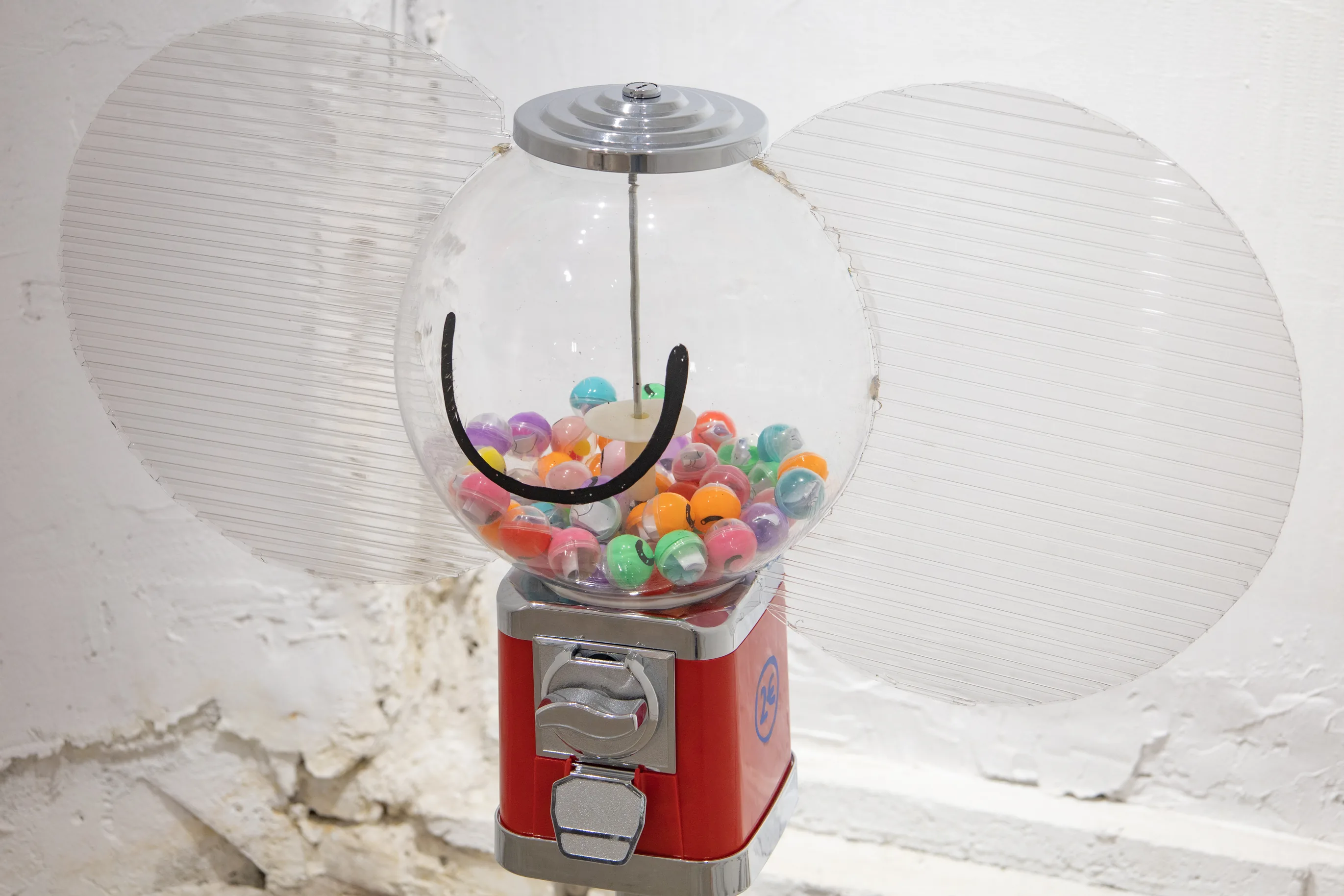 A red gumball machine full of colorful capsules in front of two translucent round panels